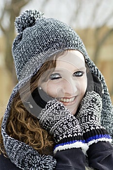 Happy teenage girl outdoors wearing black and white winter hat and mittnes