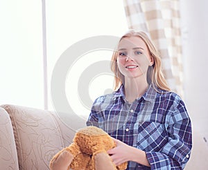 Happy teenage girl playing with Teddy Bear sitting on sofa. We are happy to regain our childhood.