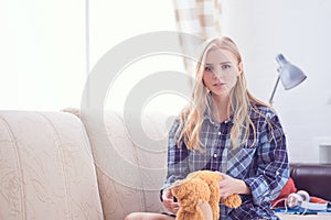 Happy teenage girl playing with Teddy Bear sitting on sofa. We are happy to regain our childhood.