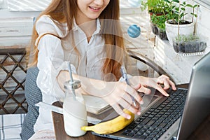 Happy teenage girl sits in her pajamas and learns remotely via the Internet during quarantine. On the table are