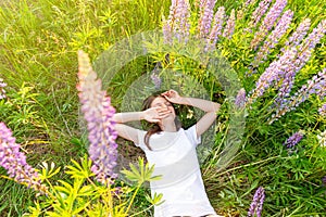 Happy teenage girl smiling outdoor. Beautiful young teen woman resting lying on summer field with blooming wild flowers