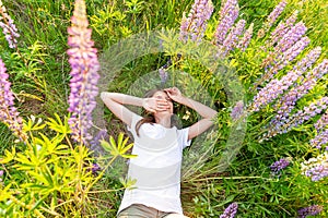 Happy teenage girl smiling outdoor. Beautiful young teen woman resting lying on summer field with blooming wild flowers