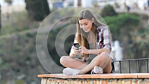 Happy teenage girl texting on phone in a town