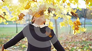 Happy teenage girl throws up leaves in autumn park