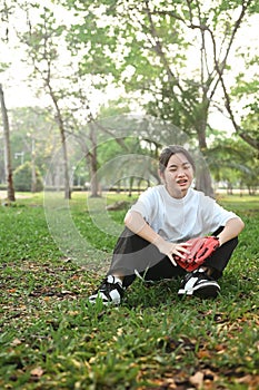 Happy teenage girl wearing leather baseball glove sitting on green lawn during summer day