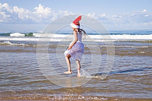 Happy teenage girl wearing a red Santa hat running through the sea water on clear sunny day