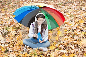 Happy teenage kid wearing earphones listen music and read book in autumn forest with beautiful seasonal nature under