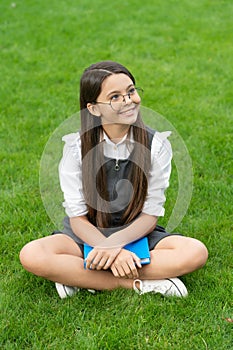 Happy teenage school girl sitting legs crossed on grass. School and education. Back to school