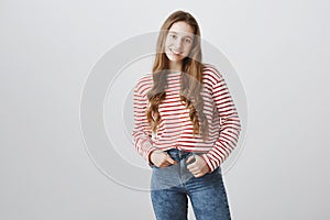 Happy teenage years. Portrait of young pretty blonde girl in trendy striped sweater holding hand in pocket and smiling