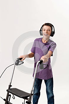 Happy teenaged disabled boy with cerebral palsy in headphones smiling at camera, taking steps with his walker isolated