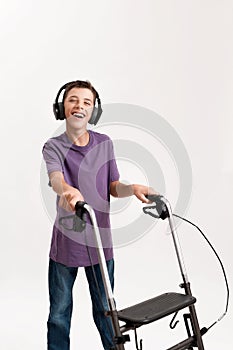 Happy teenaged disabled boy with cerebral palsy in headphones smiling at camera, taking steps with his walker isolated