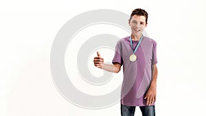 Happy teenaged disabled boy with cerebral palsy wearing gold medal, smiling and showing thumbs up at camera, standing