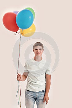 Happy teenaged disabled boy with Down syndrome smiling at camera, holding a bunch of colorful balloons while standing