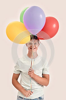 Happy teenaged disabled boy with Down syndrome smiling at camera, holding a bunch of colorful balloons while standing