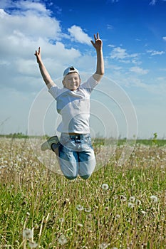 Happy teenager boy jumps at meadow