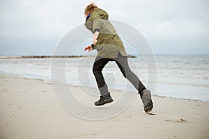 Happy teenager boy running on water of Baltic sea at cold and windy weathe
