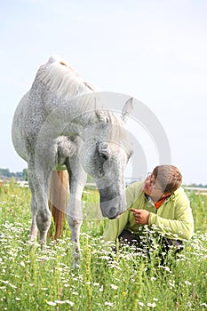 Happy teenager boy and white horse at the field