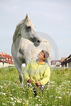 Happy teenager boy and white horse at the field