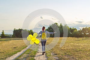 Happy teenager girl with balloons running and jumping along country road