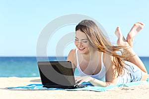 Happy teenager girl browsing social media in a laptop on the beach photo