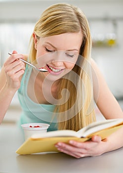 Happy teenager girl reading book and eating yogurt