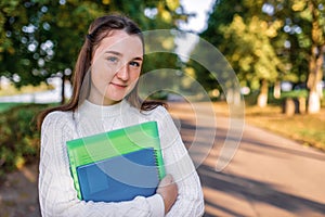 Happy teenager girl smiling, standing in summer park, autumn trees background, free space copy text. In hands notebook