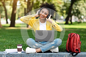 Happy Teenager Girl Using Laptop Computer Wearing Headphones In Park