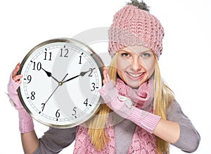 Happy teenager girl in winter hat and scarf showing clock