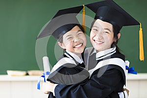 Happy teenager in graduation gowns hugging and smiling