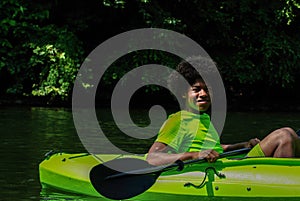 Happy teenager kayaking with paddle on scenic river with copy space