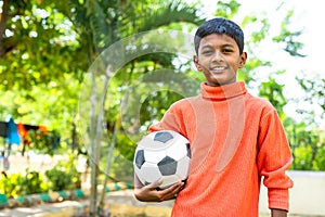 Happy teenager kid holding football by looking camera at garden with copy space - concept of childhood lifestyle, future