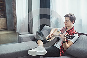 happy teenager playing acoustic guitar on sofa photo