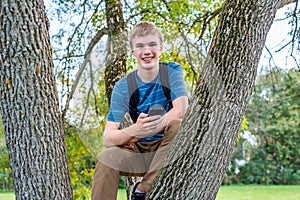 Happy teenager sitting in a tree with his cellphone.