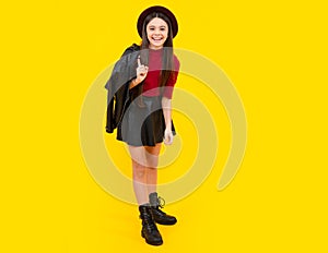 Happy teenager smiling girl. Teenager child girl casual leather skirt posing isolated on yellow background in studio