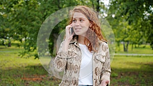 Happy teenager talking on mobile phone in green park gesturing having fun