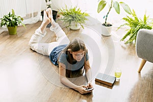 A happy teenager is texting on a mobile phone, lying on the floor in the living room. Modern technologies, online