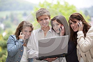 Happy teenagers with cellphones and a laptop