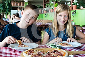 Happy teenagers eating pizza in a cafe. Friends or siblings having fun in restaurant