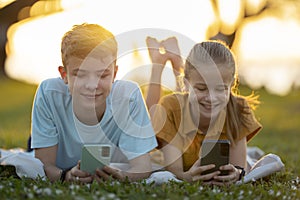 Happy teenagers girl and boy messaging on their cellphones outdoors in summer park