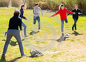 Happy teenagers playing football on green lawn