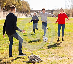 Happy teenagers playing football on green lawn