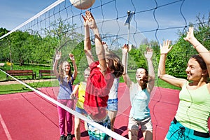 Happy teens with arms up play volleyball near net