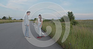 Happy teens having joyful talk during a walk with skateboard out of city