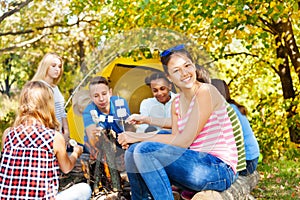 Happy teens hold marshmallow sitting on campsite