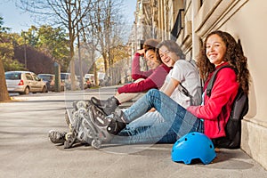 Happy teens with rollerblades sitting at sidewalk