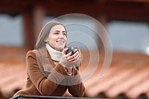 Happy tenant drinking coffee in a balcony in winter