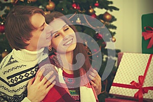 Happy tender loving couple in embrace warmed at Christmas tree