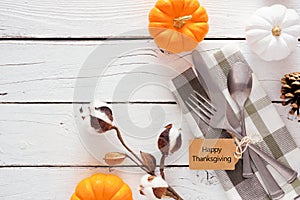 Happy Thanksgiving gift tag with silverware, check print napkin, pumpkins and decor over a white wood background