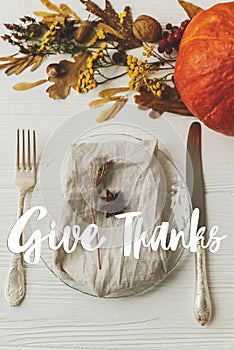 Happy Thanksgiving greeting card. Give Thanks text handwritten on thanksgiving table setting, plate, linen, anise, autumn leaves,
