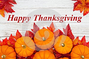 Happy Thanksgiving greeting with red and orange fall leaves and a pumpkins on weathered wood